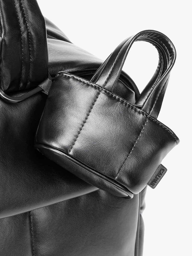 Closeup of a small Black CALPAK Luka Tote Bag Charm with dual top handles and a black carabiner clip attached to the side, shown against a plain white background