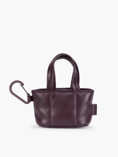 A small deep burgundy Dark Cherry CALPAK Luka Tote Bag Charm with dual top handles and a black carabiner clip attached to the side, shown against a plain white background; AMT2601-DARK-CHERRY-PU view 1