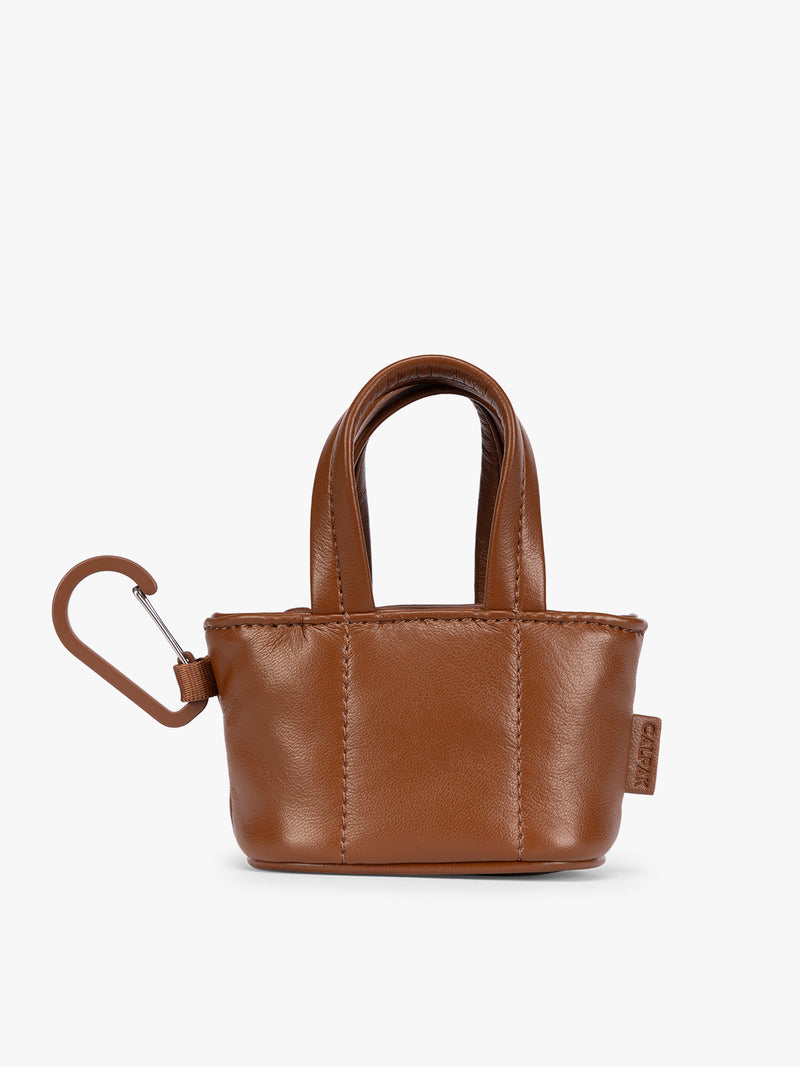 A small light brown Honey Brown CALPAK Luka Tote Bag Charm with dual top handles and a black carabiner clip attached to the side, shown against a plain white background