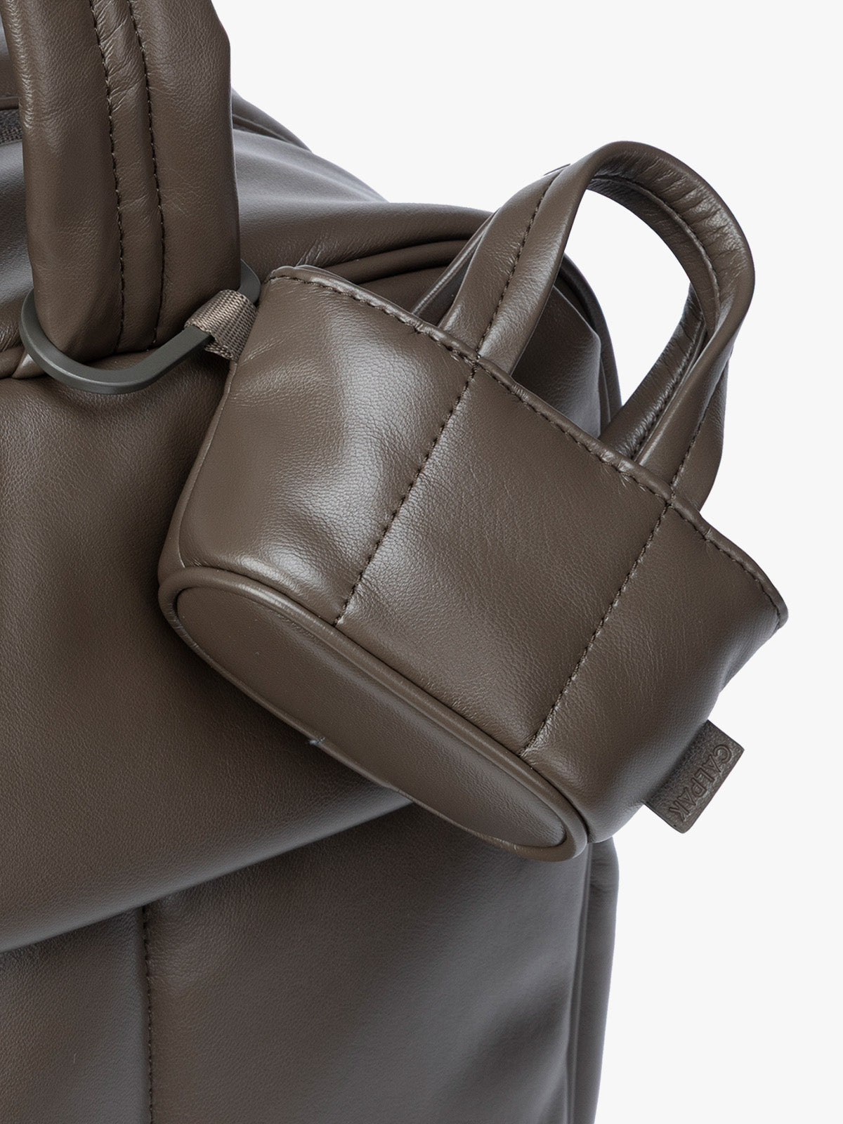 Closeup of A small dark brown Mushroom CALPAK Luka Tote Bag Charm with dual top handles and a black carabiner clip attached to the side, shown against a plain white background; AMT2601-MUSHROOM-PU