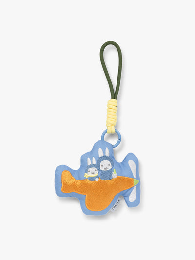 Plush Miffy x CALPAK Pluffy Bag Charm keychain with a blue border and Miffys holding a carrot on an orange airplane with a white background;APLF2501-MIFFY-ON-THE-WAY view 1