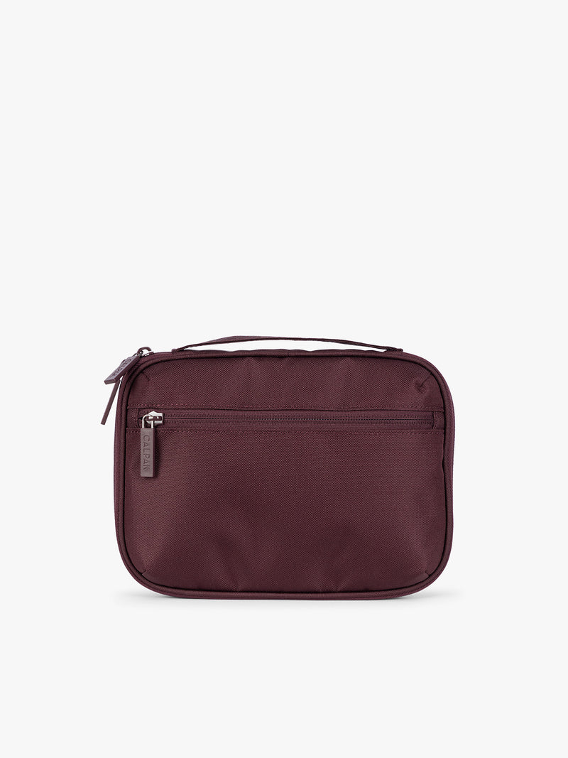 Backside of a dark burgundy CALPAK Tech Organizer pouch with a top zipper, front zippered pocket, and a small silver metal brand zipper, shown against a plain white background
