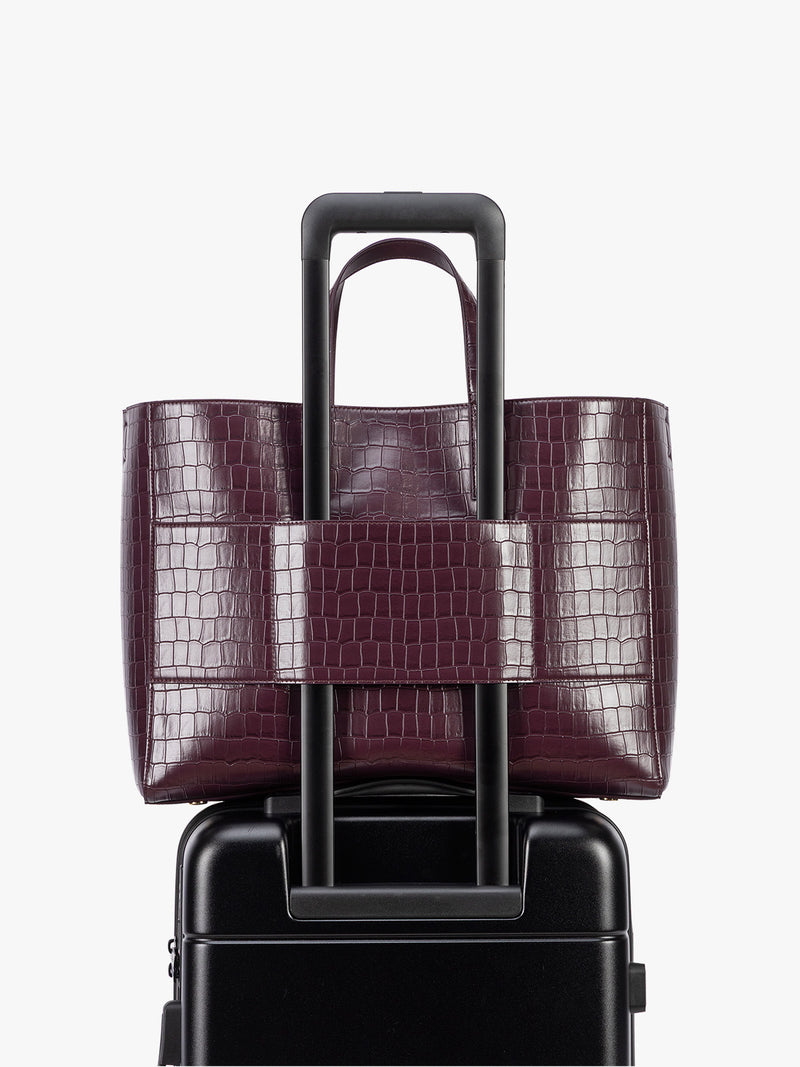 Backside luggage trolley sleeve of CALPAK Haven 16" Laptop Tote in Dark Cherry deep red crocodile-embossed tote bag with top handles and a detachable shoulder strap, shown against a plain white background