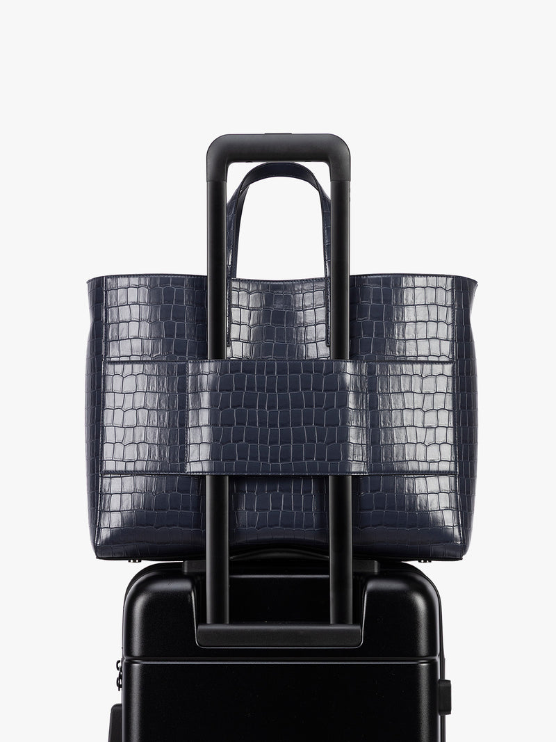 Backside luggage torlley sleeve of CALPAK Haven 16" Laptop Tote in blue Navy crocodile-embossed tote bag with top handles and a detachable shoulder strap, shown against a plain white background