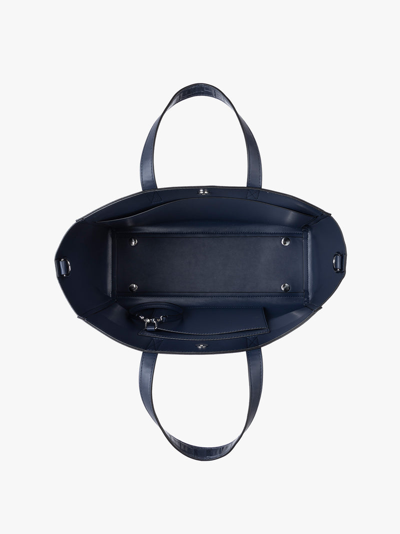 Top down view of a navy CALPAK Haven 15" Laptop Tote in Navy blue crocodile-embossed with dual top handles and a matching shoulder strap against a plain white background