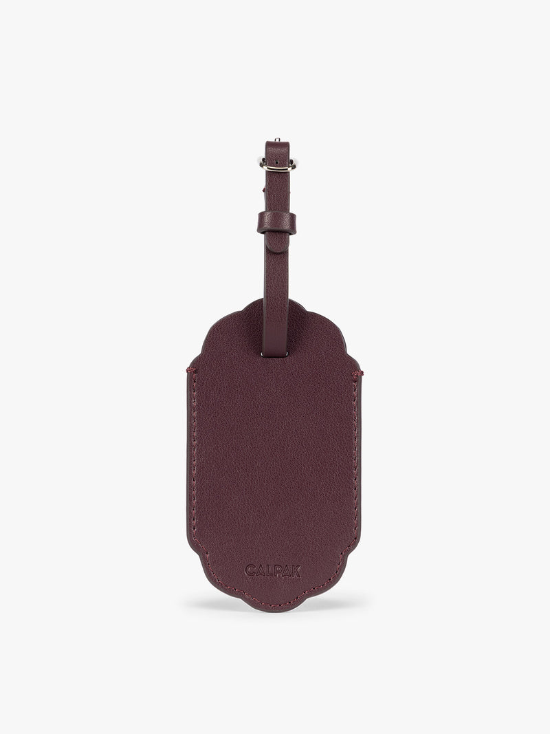 Back side of dark red CALPAK Vault luggage tag with a scalloped border and a matching honey dark red , shown against a plain white background
