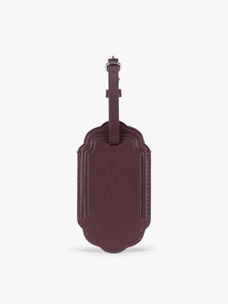 A dark red CALPAK Vault luggage tag with a scalloped border and a matching honey dark red , shown against a plain white background