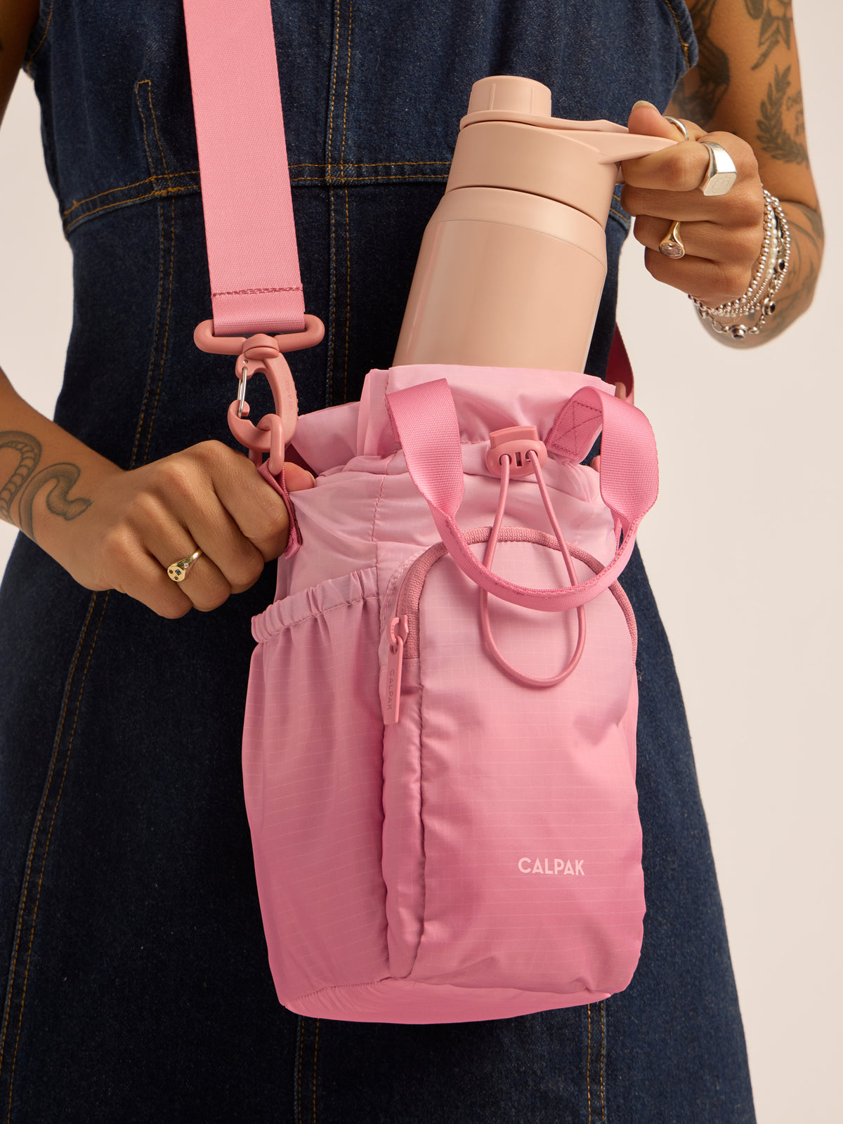 Model inserting water bottle into the CALPAK Water Bottle Holder in pink ombre Tea Rose; AWH2101-TEA-ROSE