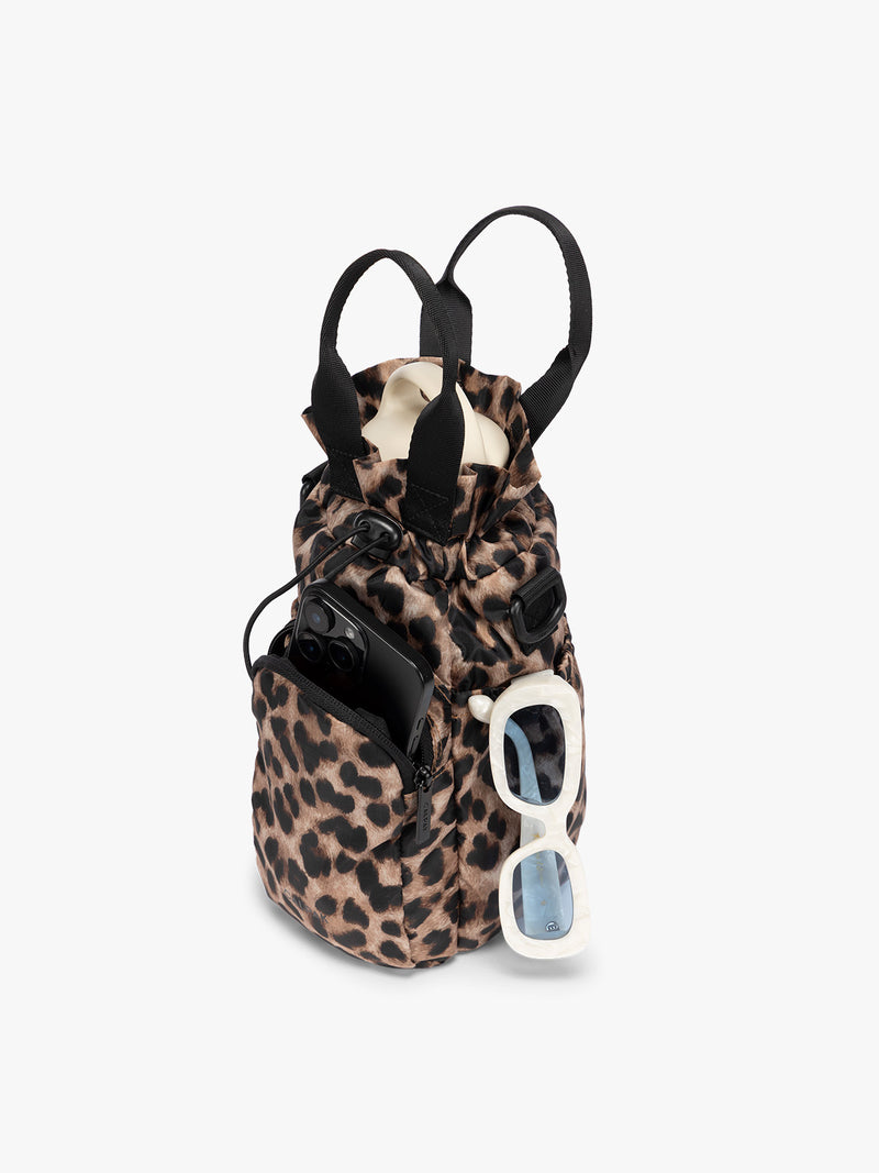water bottle, phone and sunglasses in a  tan and black animal print Leopard CALPAK Water Bottle Holder with top handles, drawstring top, front zippered pocket, and a detachable shoulder strap with an expandable top
