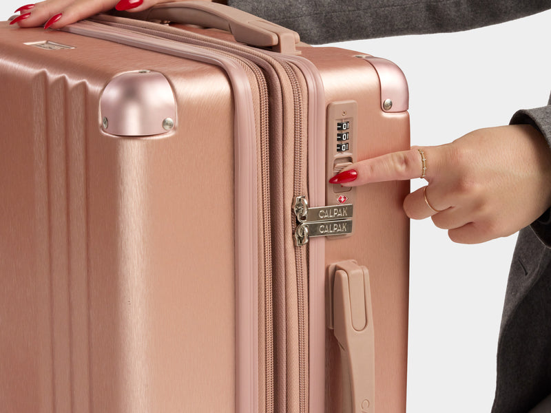 Model pointing at the CALPAK Ambeur Luggage Collection TSA approved lock in Rose Gold