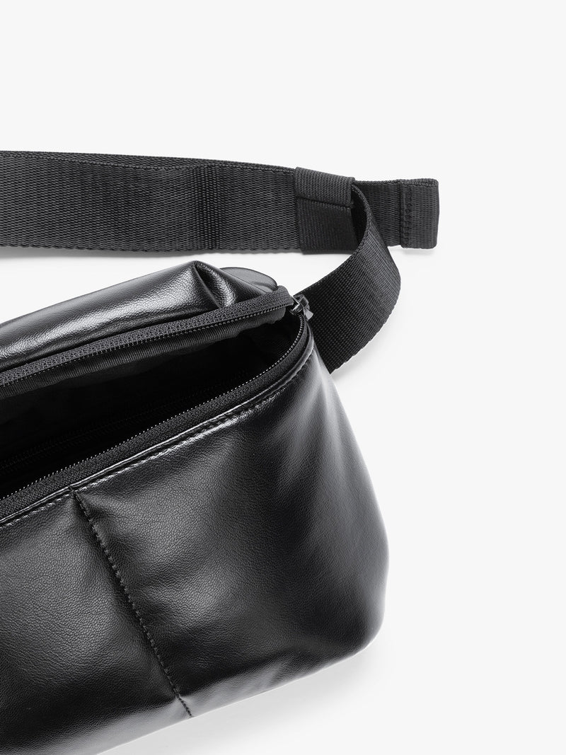 Close up of front zipper and crossbody strap of a black vegan leather CALPAK Luka Belt Bag with a zippered front pocket and side straps, shown against a plain white background