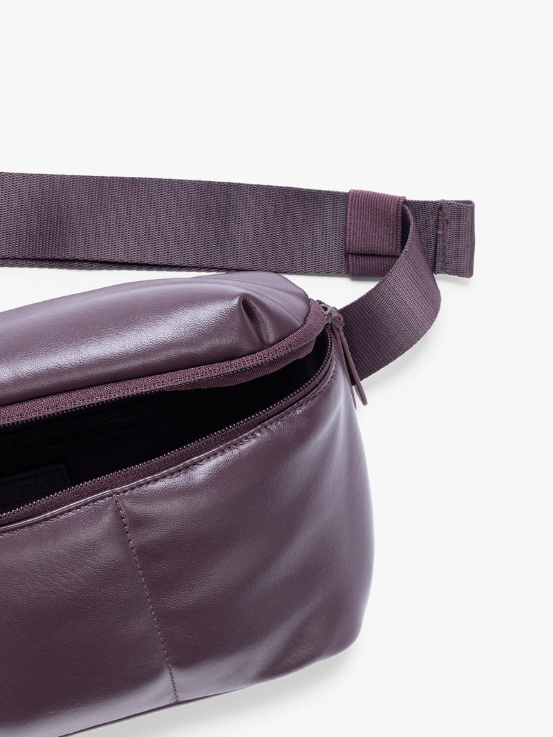 Closeup of front zipper pocket with crossbody strap of a deep burgundy Dark Cherry vegan leather CALPAK Luka Belt Bag with a zippered front pocket and side straps, shown against a plain white background