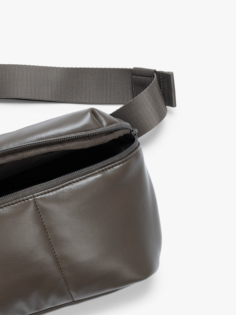 Close up of front pocket zipper and crossbody strap of a dark brown Mushroom vegan leather CALPAK Luka Belt Bag with a zippered front pocket and side straps, shown against a plain white background