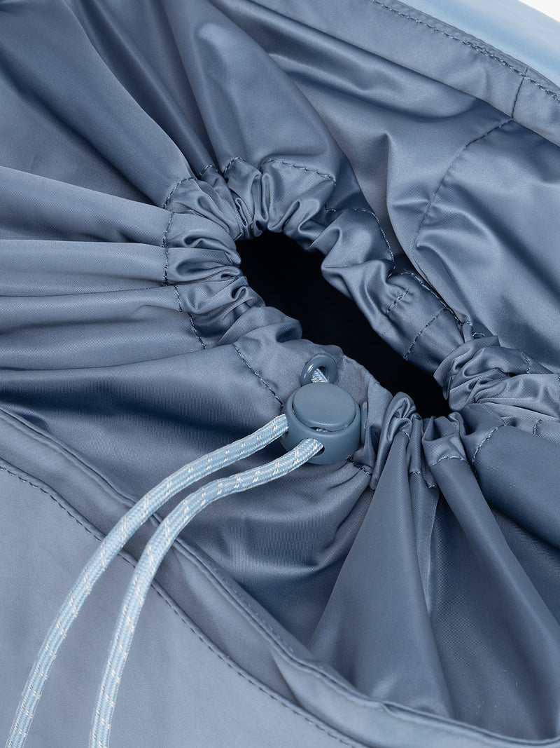 Close-up of a gray drawstring bag with a button closure of CALPAK Fit Gym Backpack in blue Indigo with white background