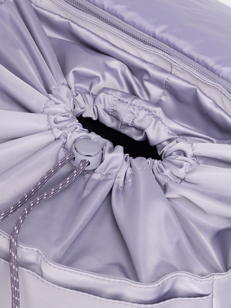 Model using drawstring closing feature of CALPAK Fit Gym Backpack in light purple Iris front view with white background