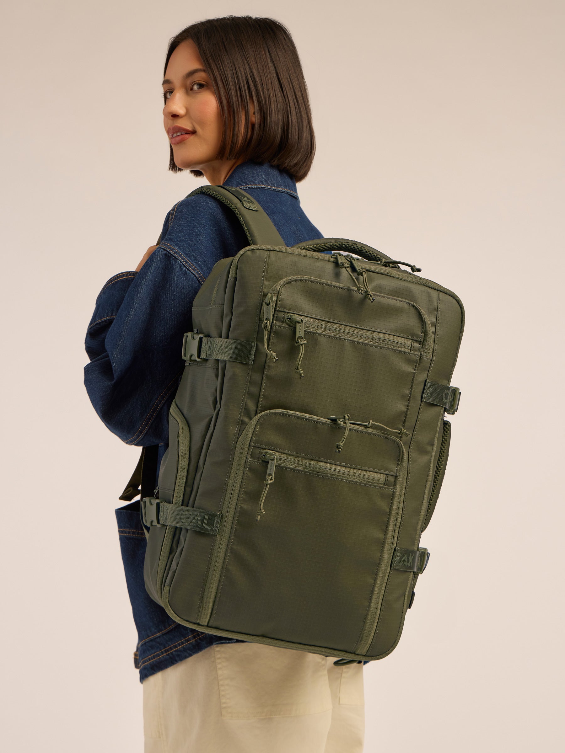 Model wearing the CALPAK Terra 26L Laptop Backpack Duffel in dark green Matte Pine; BPH2201-PINE