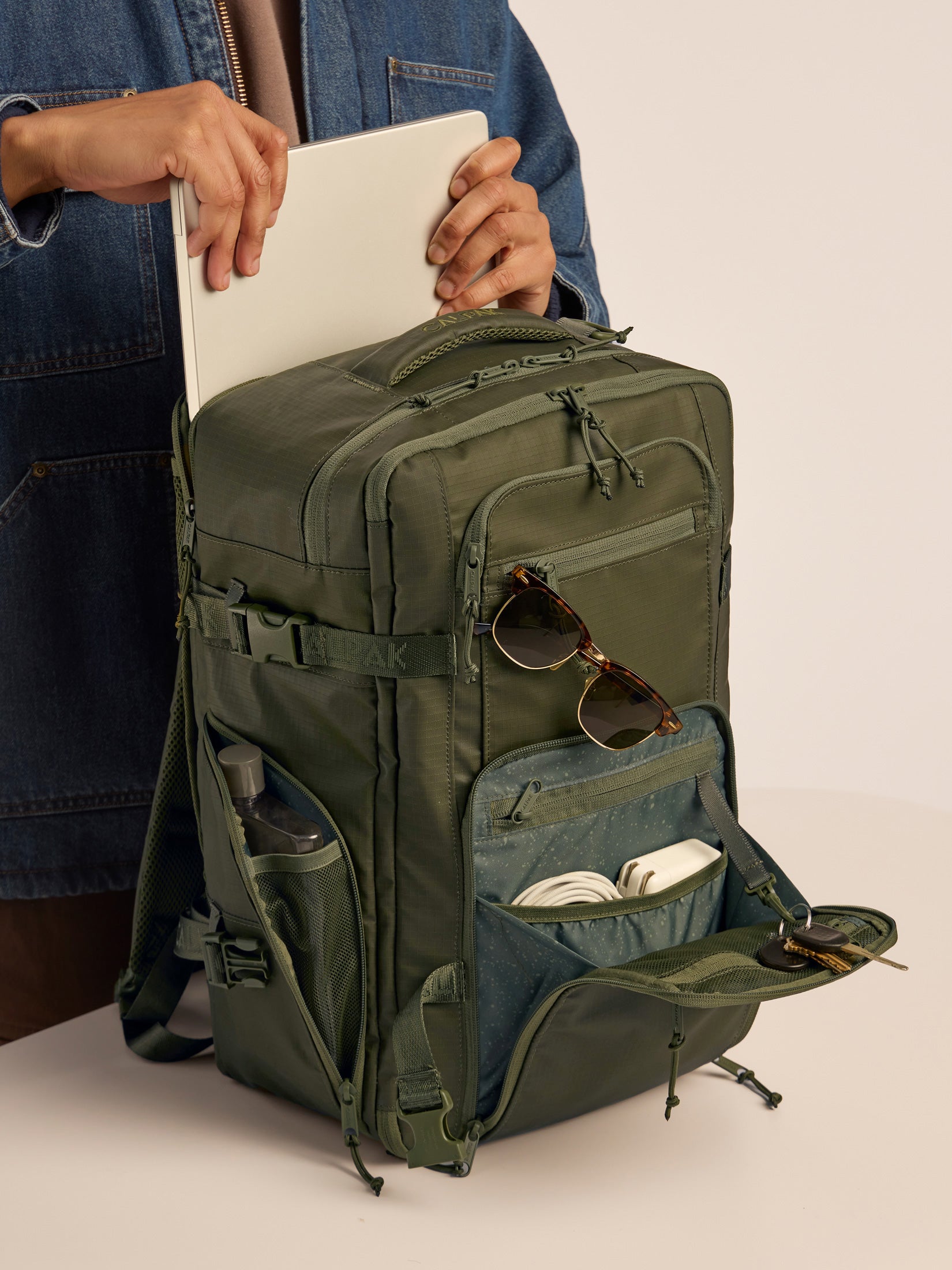 Model putting in laptop into the CALPAK Terra 26L Laptop Backpack Duffel in dark green Matte Pine duffel; BPH2201-PINE