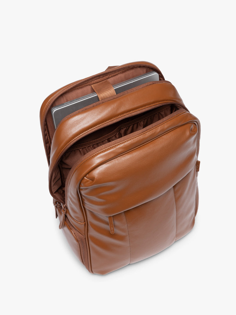 Laptop sleeve of CALPAK Honey Brown Luka 15 inch Laptop Backpack in vegan leather with a glossy finish, featuring a top carry handle, a main zippered compartment, and a front slip pocket, shown against a plain white background