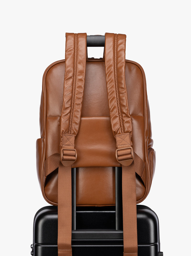 Backside luggage trolley sleeve of CALPAK Honey Brown Luka 15 inch Laptop Backpack in vegan leather with a glossy finish, featuring a top carry handle, a main zippered compartment, and a front slip pocket, shown against a plain white background