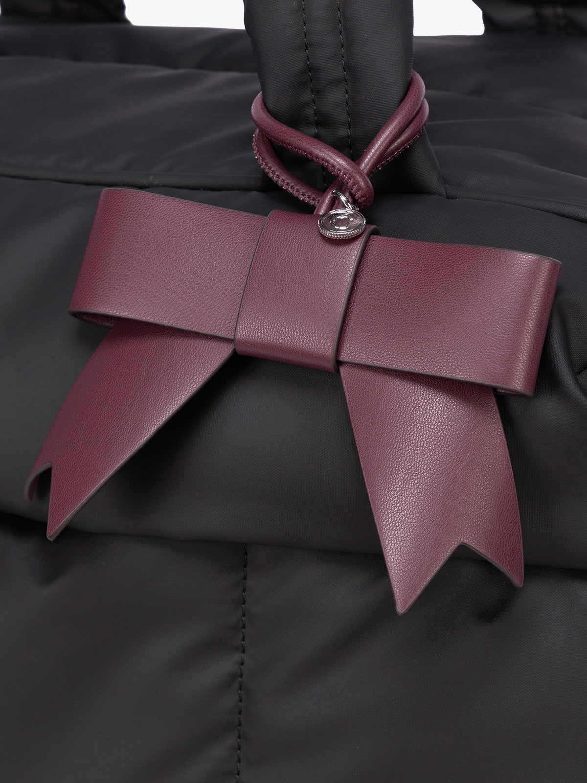 A close-up of a burgundy Dark Cherry CALPAK Personalized Bow Bag Charm with a top loop attached to a bag ; BWBC2601-DARK-CHERRY