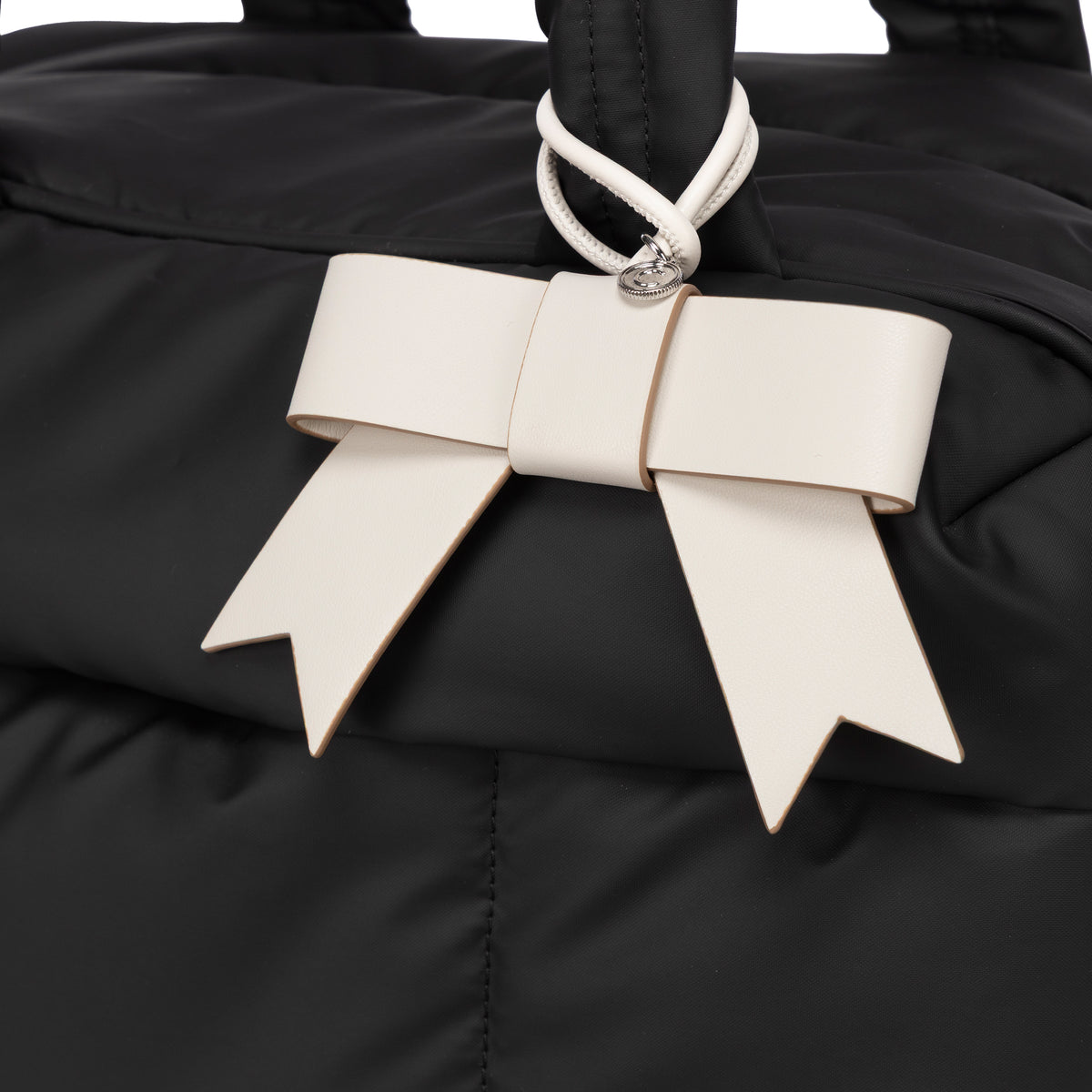 Closeup of a white Vanilla color CALPAK Personalized Bow Bag Charm with a top loop, featuring a silver-tone metal ring attached to a bag ; BWBC2601-VANILLA