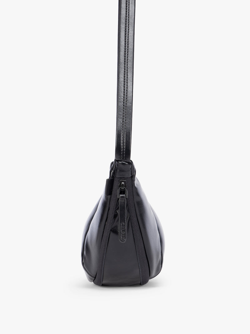 Side expandable zipper of Black vegan leather Luka Crescent shoulder bag with a long thin strap, shown against a plain light gray background