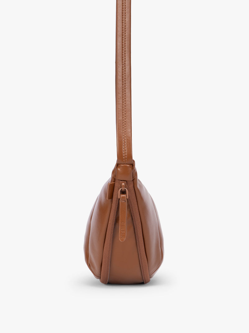 Side expandable zipper of Honey Brown vegan leather Luka Crescent shoulder bag with a long thin strap, shown against a plain light gray background