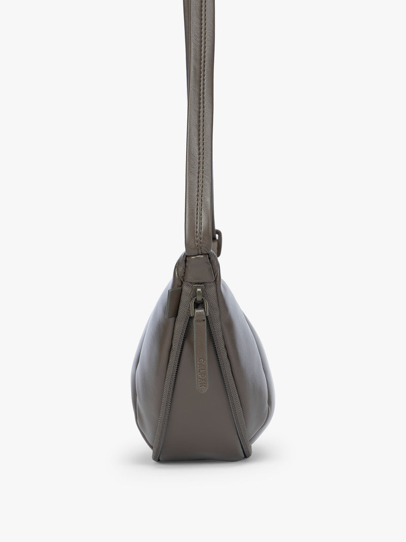 Side expandable zipper of a dark brown vegan leather Luka Crescent shoulder bag with a long thin strap, shown against a plain light gray background