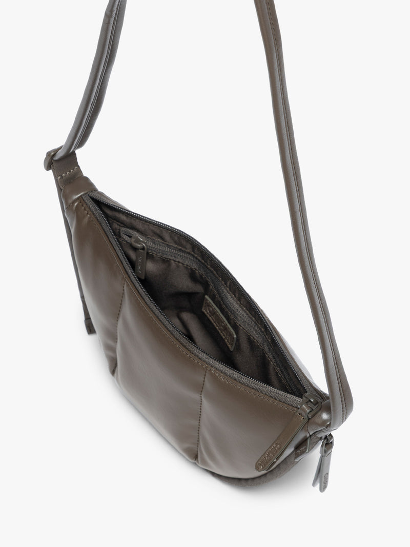 Top view of opened zipper of a dark brown vegan leather Luka Crescent shoulder bag with a long thin strap, shown against a plain light gray background