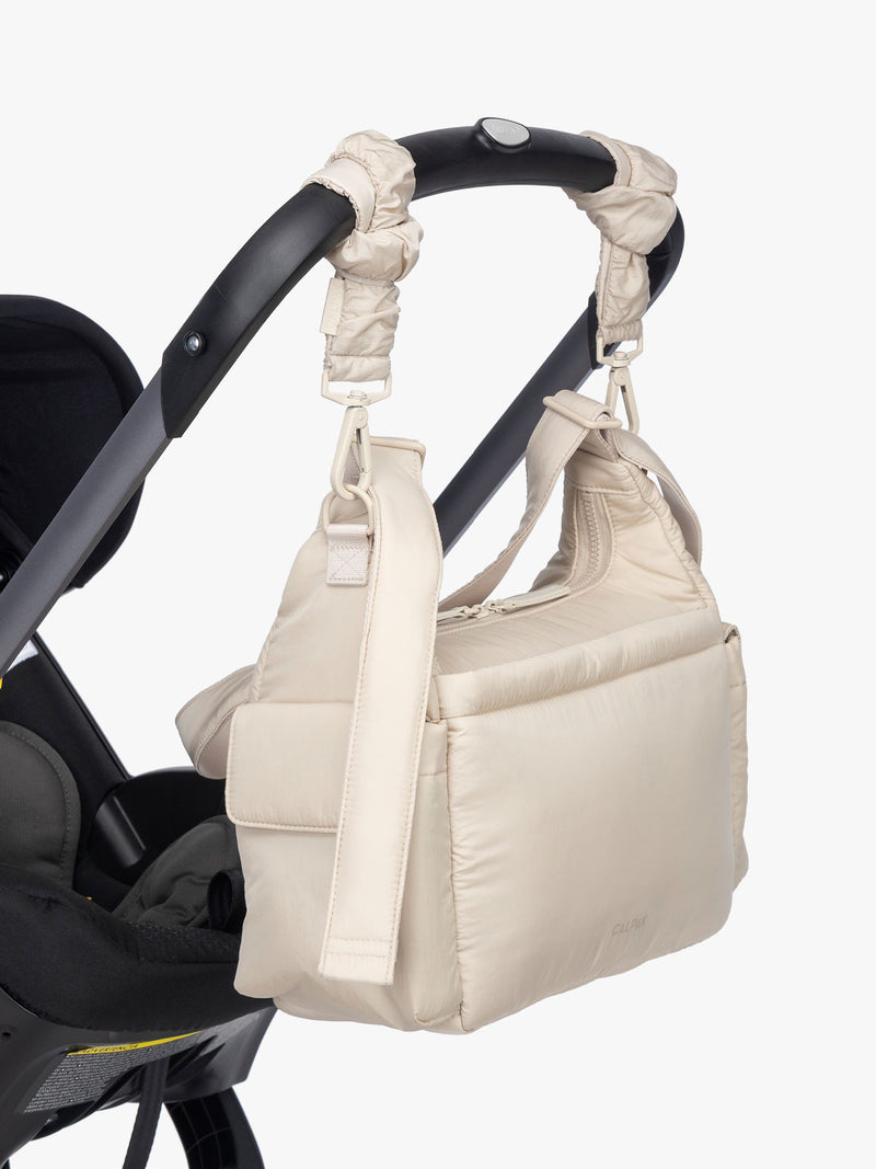 CALPAK Crossbody Diaper Bag in off-white Oatmeal strapped on stroller with Stroller Straps