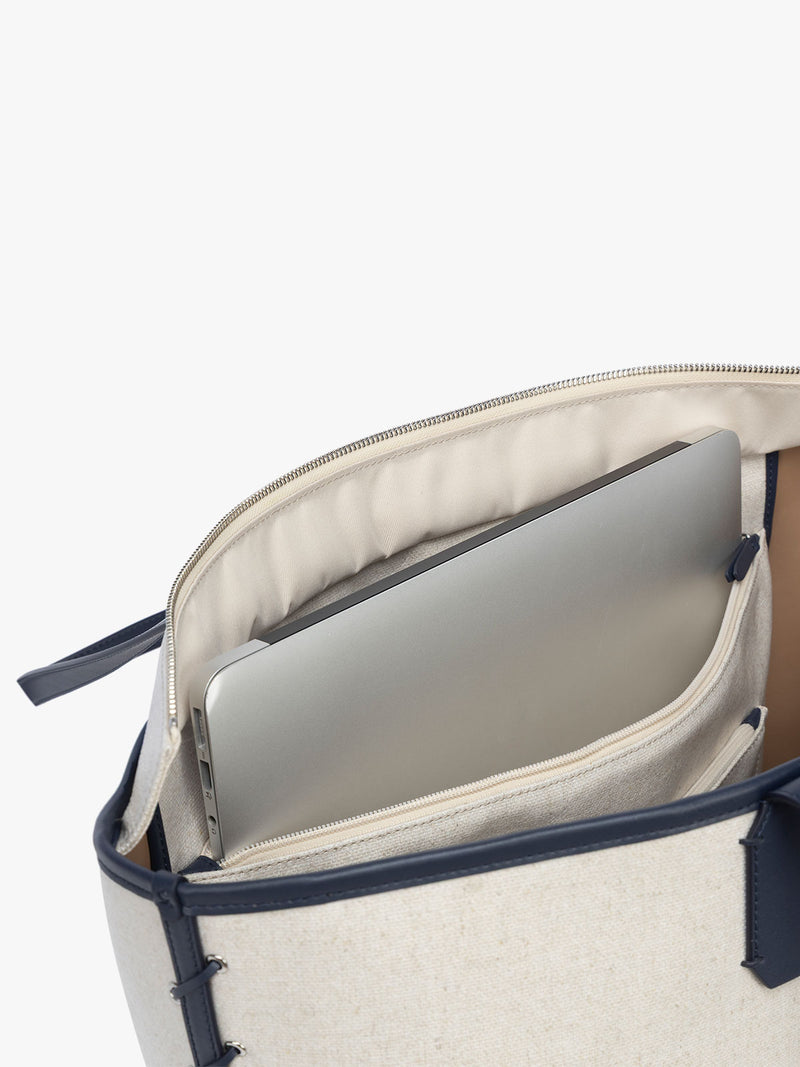 Laptop sleeve of CALPAK Colette 15" Canvas Laptop Tote with zipper and interior laptop sleeve in beige canvas material  with blue finishing in Natural Navy