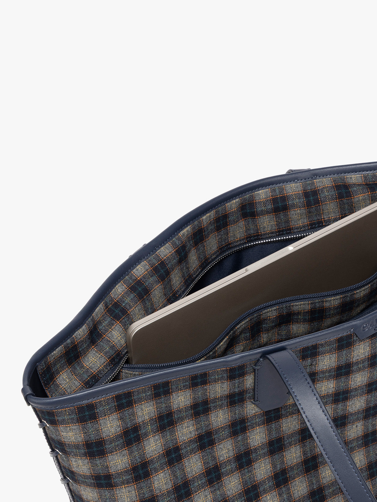 Close-up of Colette 15 Laptop Tote bag with a Navy and grey gingham pattern and dark blue leather handles in Navy interior showing a brown and beige checkered pattern lining, a zippered pocket holding a silver laptop, and dark brown leather trim against a light gray background; CLCT2601-NAVY-PLAID