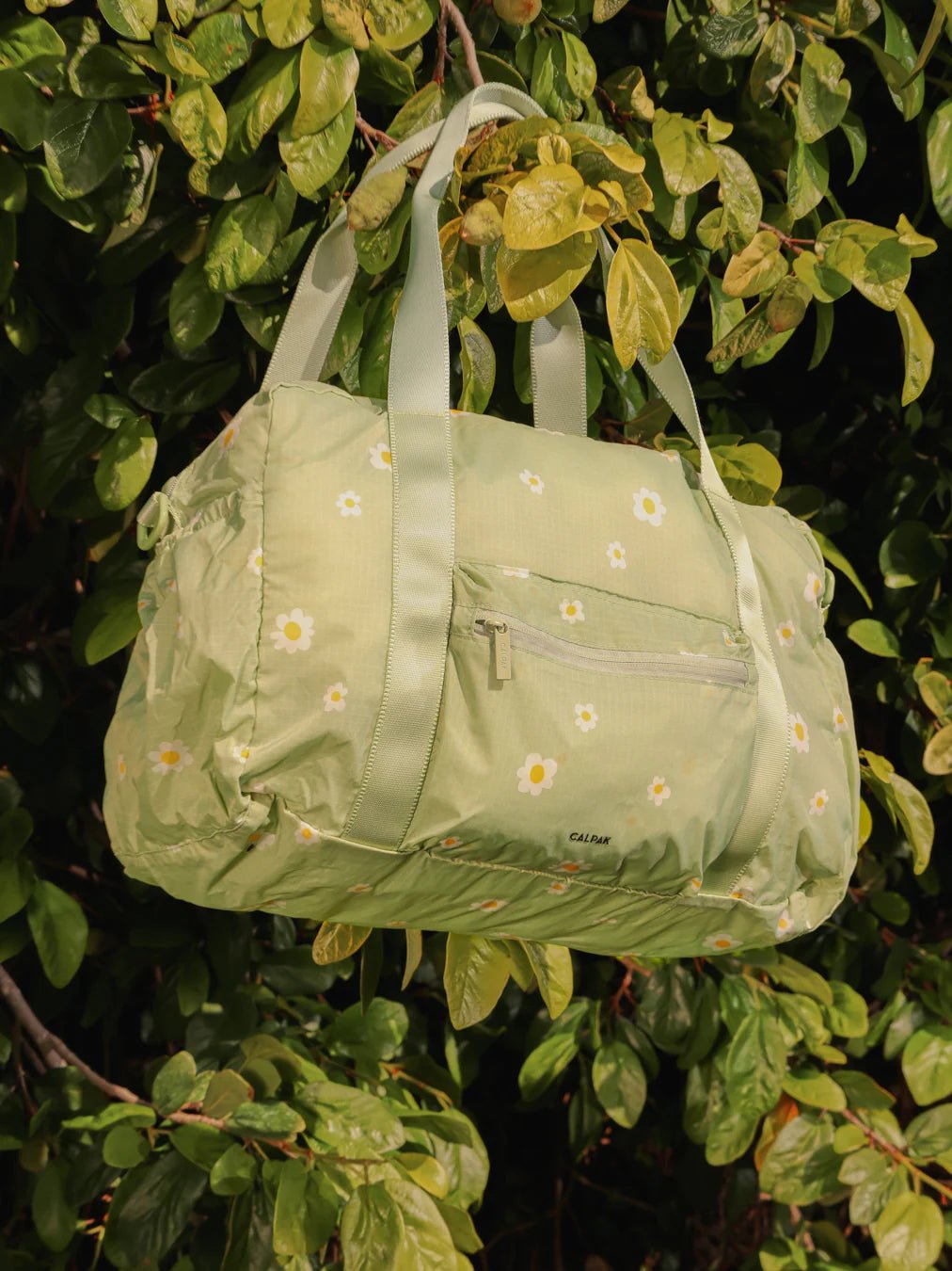 Green floral CALPAK Compakt Duffel Bag hanging in a tree
