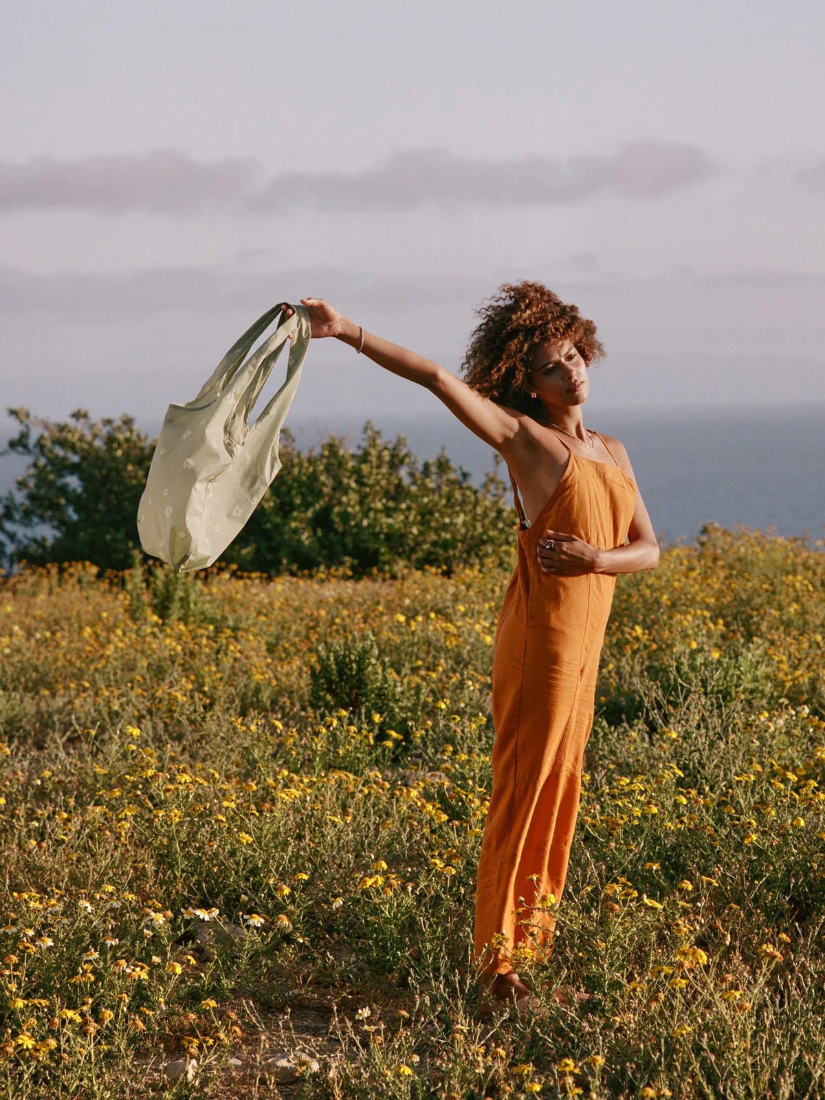 Model waving green floral CALPAK Tote Bag in the air