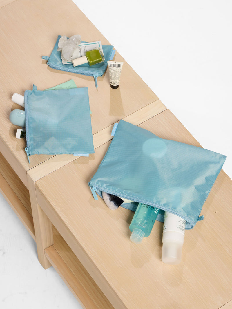 A set of translucent blue CALPAK dopp kit bags displayed on a wooden surface, filled with travel-sized toiletries and skincare essentials—ideal for those wondering what is a dopp kit and how to keep their grooming products organized.