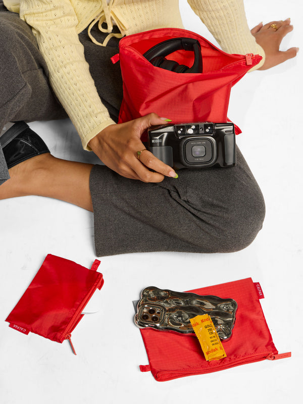 Model placing belongings inside CALPAK compakt zippered pouch set in red rouge