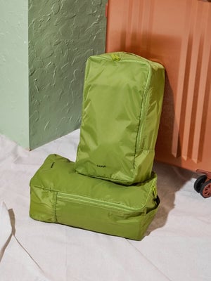 CALPAK Compakt Shoe Bag in green palm stacked on one another and leaning against CALPAK Ambeur Carry-On Luggage in copper; KSB2001-PALM