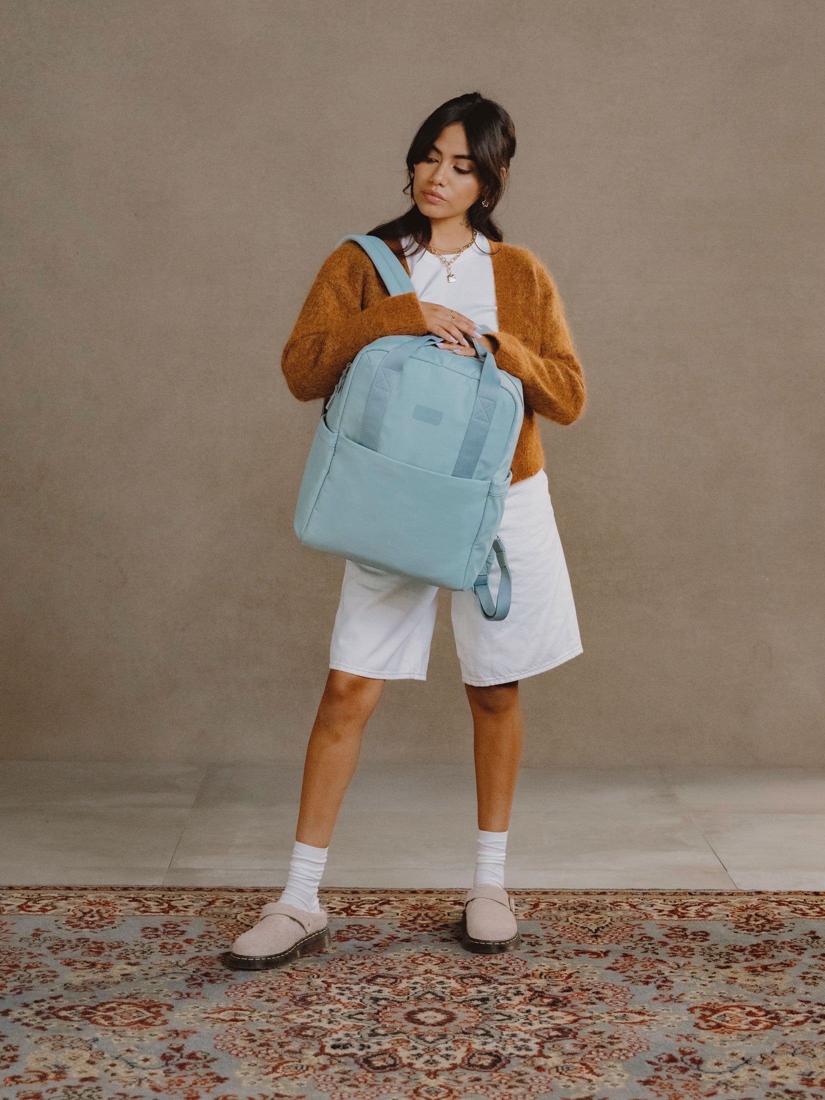 Model wearing strap of CALPAK Connect Laptop Backpack over shoulder in bluebell blue; BCN2401-BLUEBELL