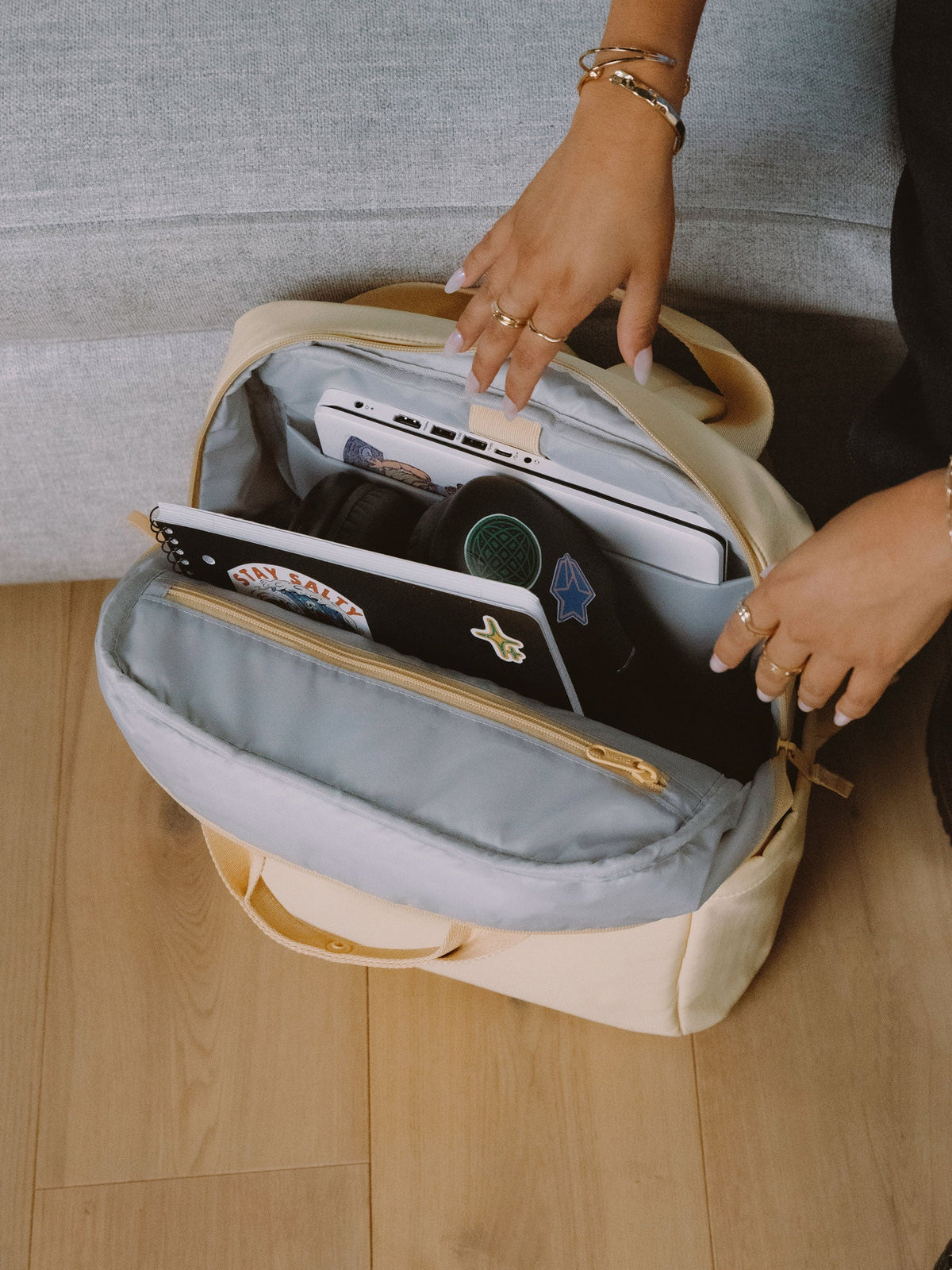 Model shows displays interior of sunshine CALPAK Connect Laptop Backpack with laptop in padded laptop sleeve and headphones and notebook in the main compartment; BCN2401-SUNSHINE