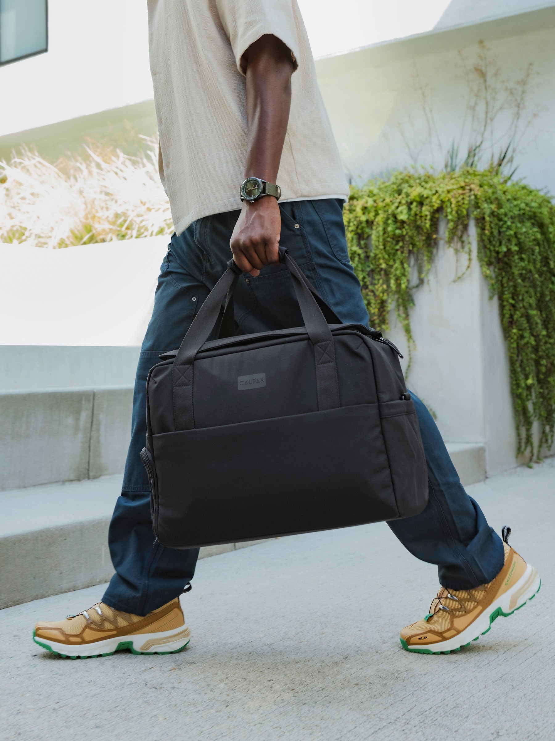 Model holding CALPAK Connect Laptop Duffel by durable carrying handles in black; DCN2401-BLACK