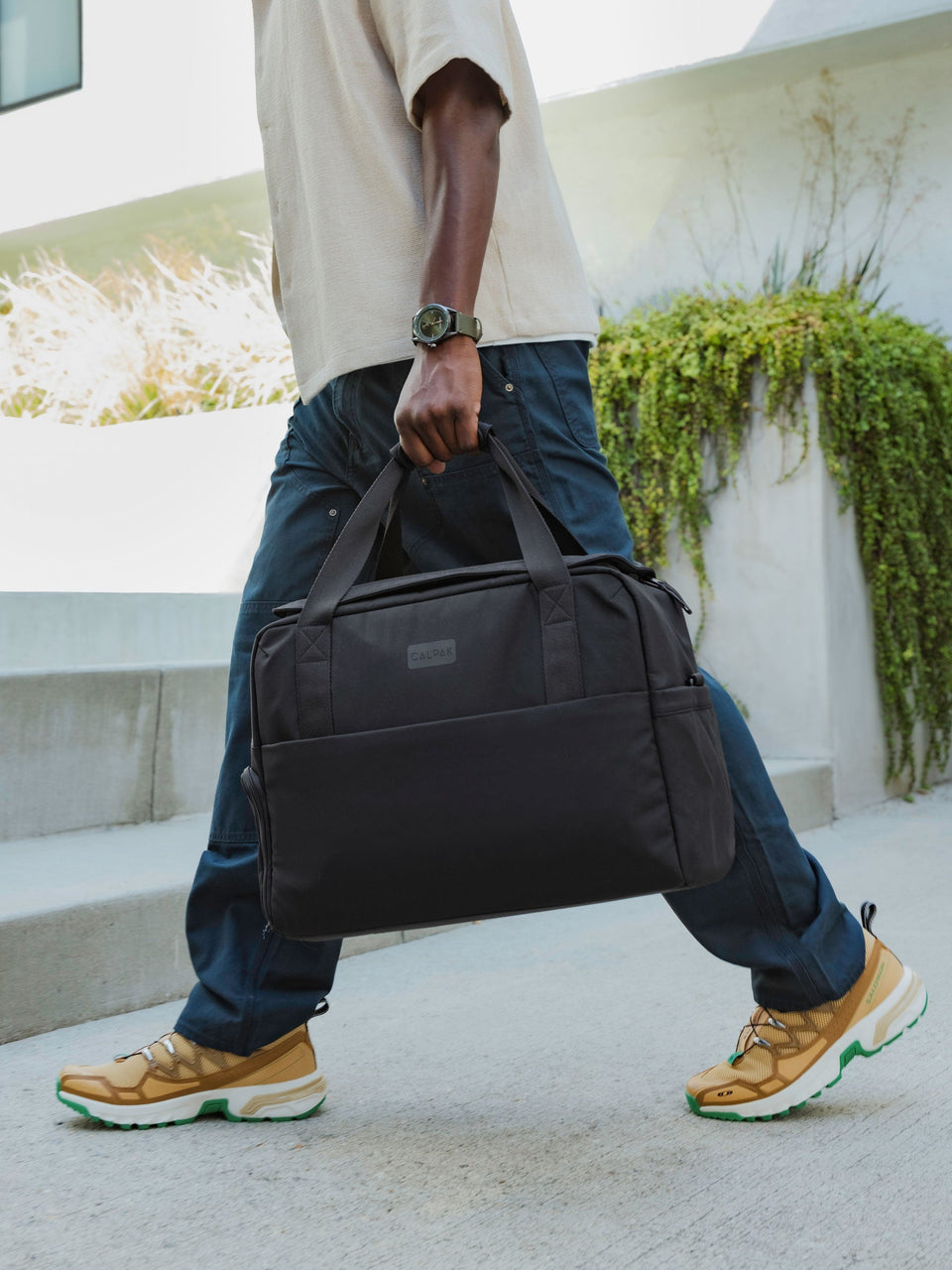 Model holding CALPAK Connect Laptop Duffel by durable carrying handles in black; DCN2401-BLACK