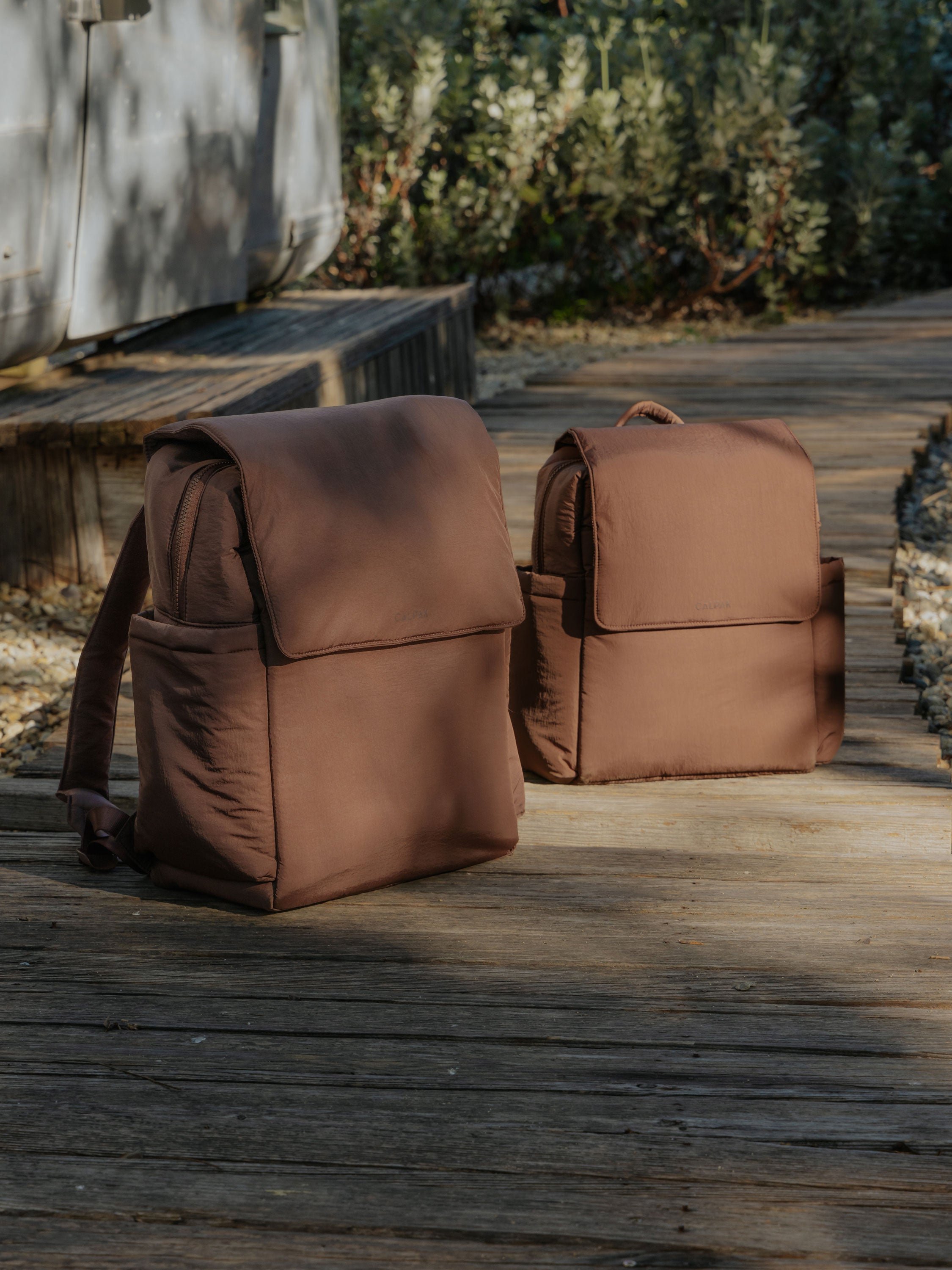 Side by side comparison of CALPAK Convertible Mini Diaper Backpack and CALPAK Diaper Backpack with Laptop Sleeve in hazelnut
