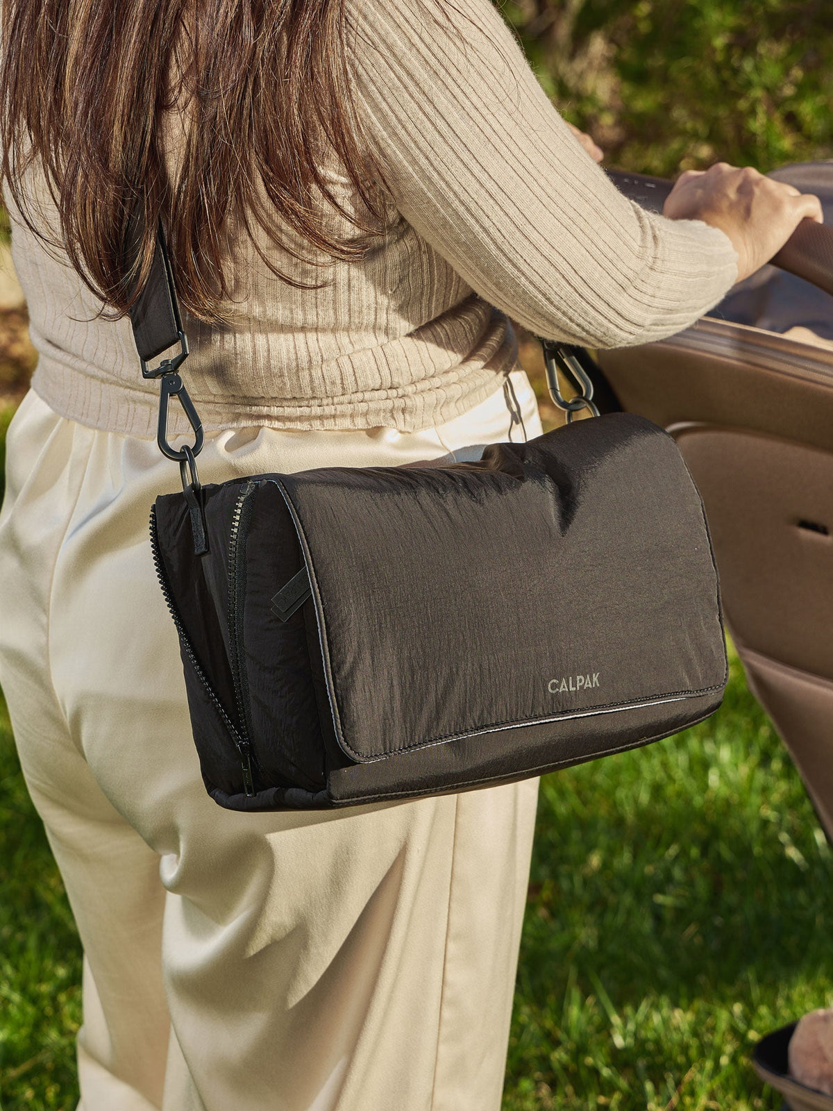 Model wearing CALPAK Convertible Stroller Caddy Crossbody as crossbody bag in black; SCB2401-BLACK