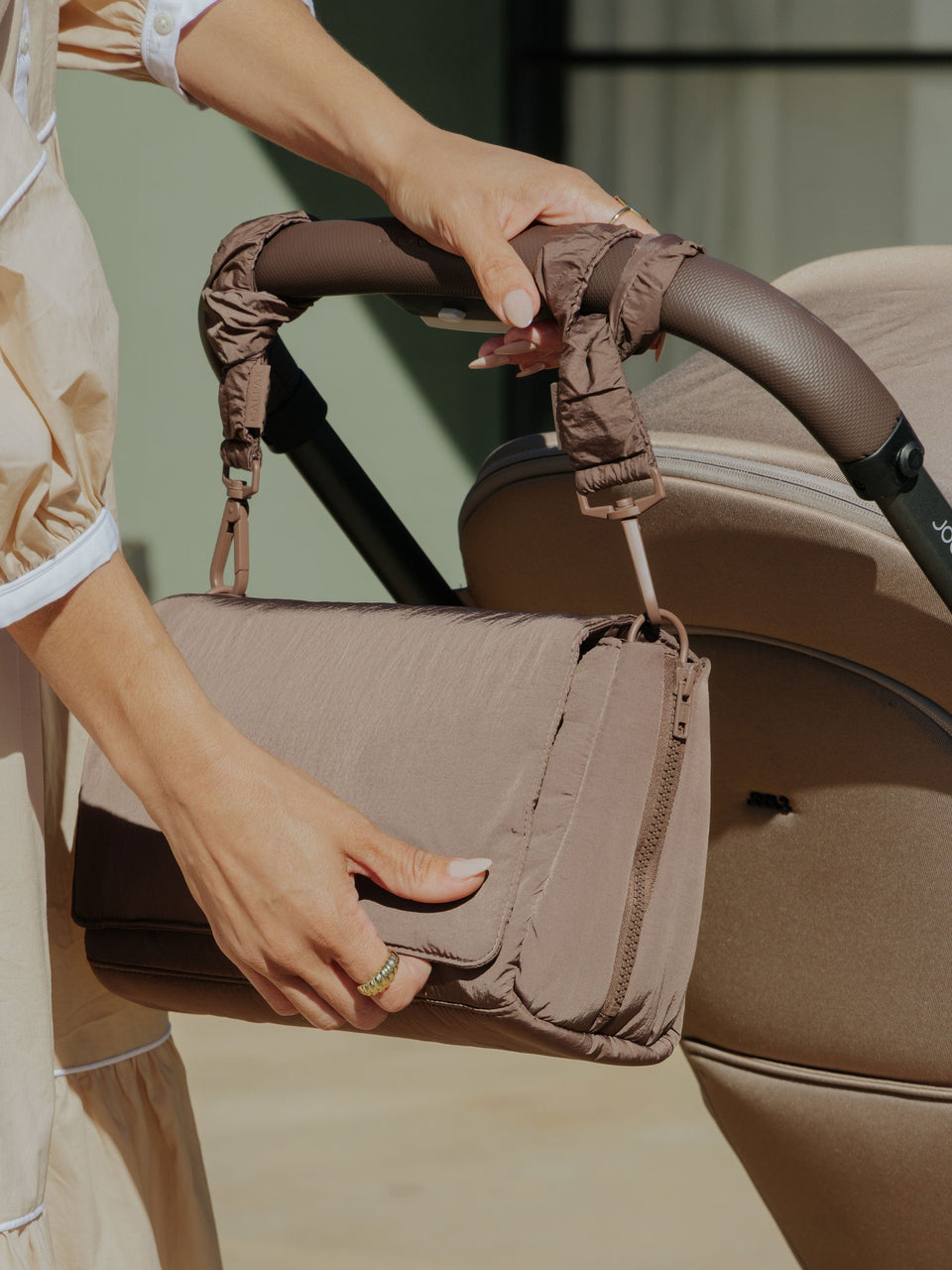 Model displaying CALPAK Convertible Stroller Caddy Crossbody attached to stroller by Stroller Straps in brown; SCB2401-HAZELNUT