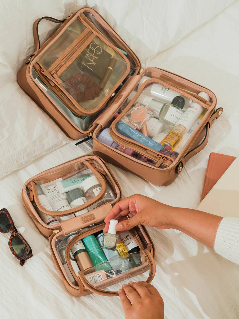 A tan CALPAK dopp kit in large and small displayed on a bed, featuring multiple compartments for organizing skincare, makeup, and grooming products—answering the question what is a dopp kit for modern travelers.