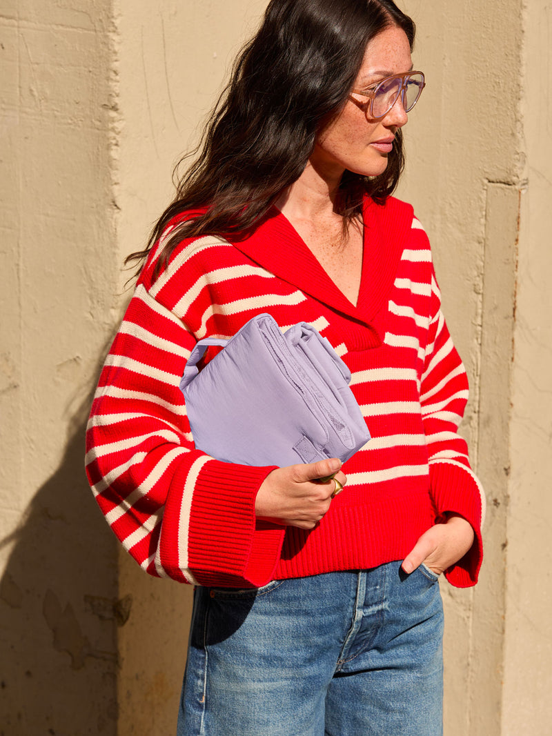 Model in red and white stripped shirt holding the CALPAK Diaper Changing Pad Organizer in lavender purple Orchid front view