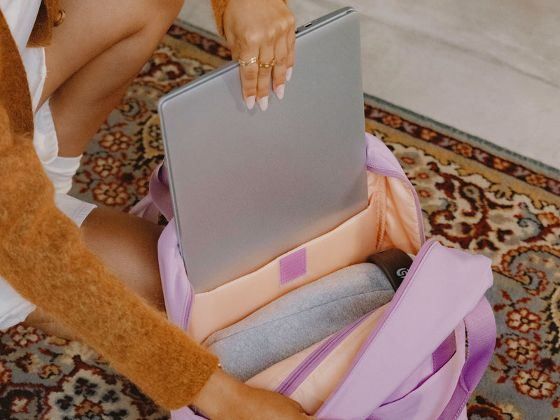 Model placing laptop in CALPAK Connect Laptop Duffel in Berry purple.