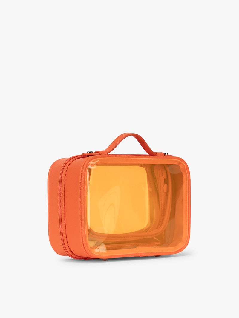 Side view of the CALPAK x Dedcool Collaboration of the Small Clear Cosmetic Case in orange Papaya with toiletry items and perfumes  on a airport chair