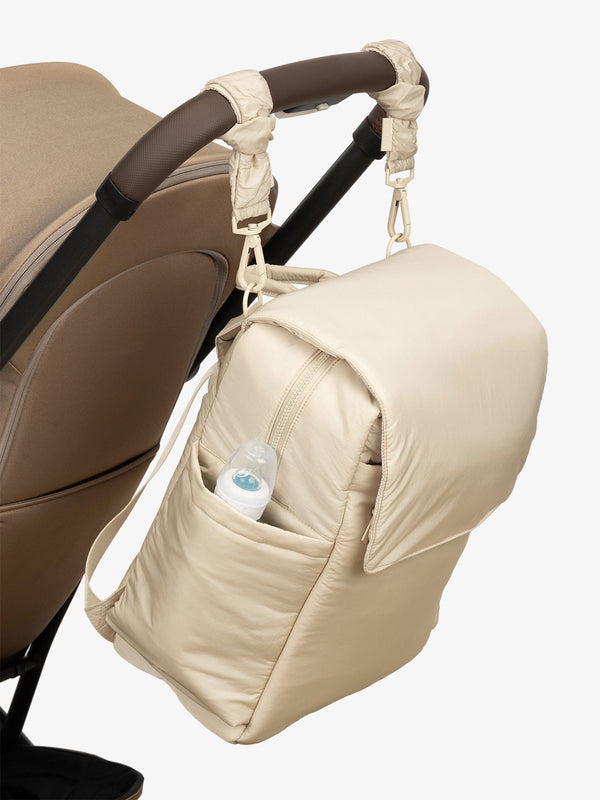 CALPAK Diaper Backpack with Laptop Sleeve attached to stroller by CALPAK Stroller Straps in oatmeal