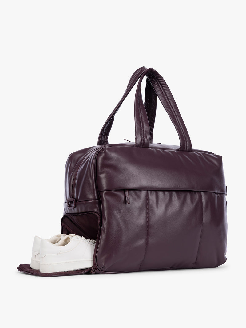 Side shoe compartment of Dark Cherry deep burgundy CALPAK Luka Large Duffel in vegan leather with dual top handles, shown against a plain white background